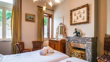 Quarto de hotel com duas camas, lareira, espelho e janela com cortinas.