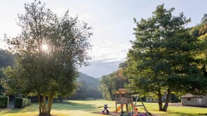 Ein Park mit Rasen, einer Spielplatzanlage, Bäumen und einer entfernten Hügellandschaft.