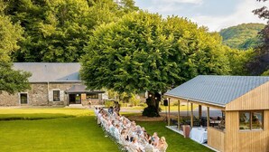 Un espace extérieur aménagé pour les repas, avec des tables et des chaises, un pavillon en bois et, au fond, un bâtiment en pierre.