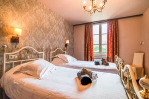 Hotellihuone, jossa on kaksi sänkyä, kattokruunu, ikkuna verhoilla ja kuviollinen tapetti yhdell ä seinällä.