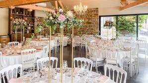 Une salle de banquet avec des chaises et des tables blanches, agrémentée de compositions florales et d’un lustre.