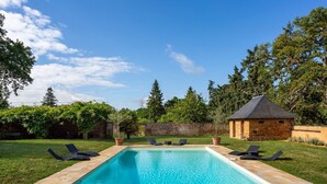 Une piscine rectangulaire bordée de pierres, entourée d’une pelouse verdoyante et d’arbres.