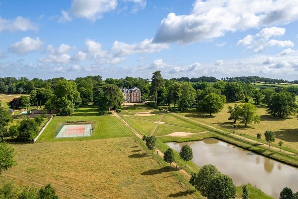 A golf course with a tennis court, a pond, and a large building in the background.