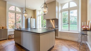 Une cuisine spacieuse dotée d’un grand îlot central, d’appareils électroménagers modernes et de grandes fenêtres offrant une vue sur l’extérieur.