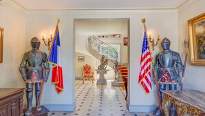 En storslagen hall med två riddarstatyer, den ena med en fransk flagga och den andra med en amerikansk flagga, som leder fram till en trappa med ett dekorativt räcke.