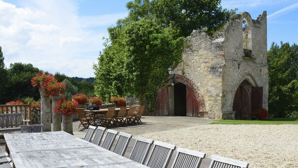 A rustic outdoor dining area with a stone building, wooden tables, and chairs.