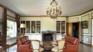 A spacious living room with leather sofas, a chandelier, a fireplace, and built-in bookcases.