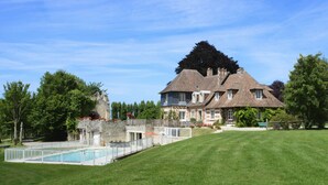 A large house with a swimming pool, surrounded by a well-maintained lawn and trees.