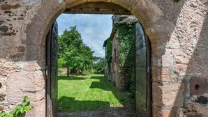 An arched stone doorway leading to a grassy courtyard with trees and a building in the background.