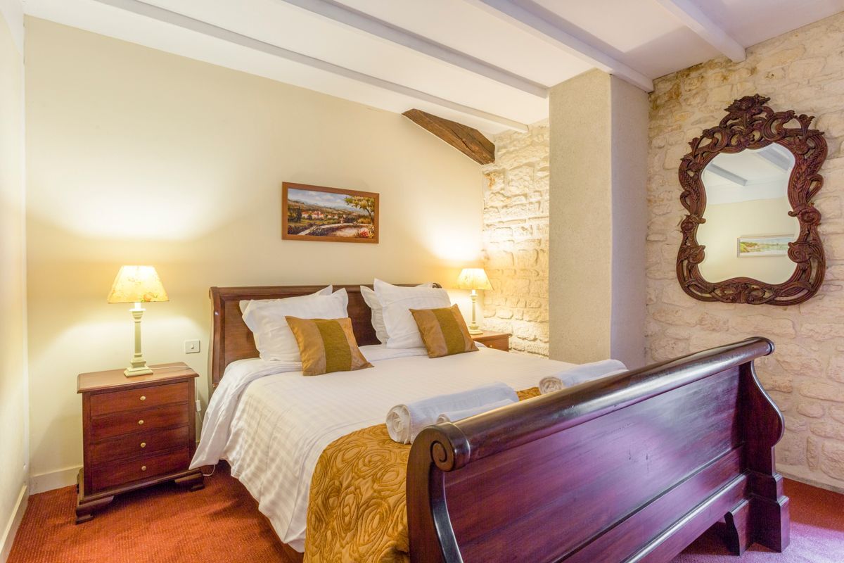 A bedroom with a wooden bed, two bedside tables with lamps, a stone wall, and a large mirror.