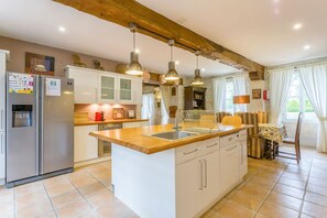 A kitchen with a central island, white cabinets, a stainless steel refrigerator, pendant lights, and a dining area with a table and chairs.