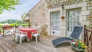 Un bâtiment en pierre doté d’une terrasse en bois, d’une table avec des chaises et d’une chaise longue.