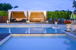 Un espace piscine doté d’un coin salon abrité, de chaises longues et de plantes en pot.