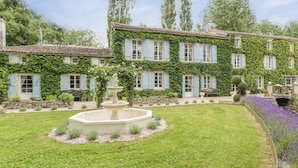 Un bâtiment à deux étages dont les murs sont recouverts de lierre et qui possède une fontaine dans la cour.
