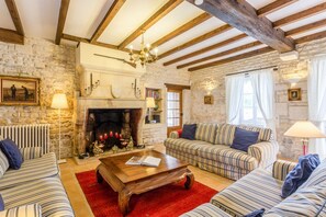 A cozy living room with a fireplace, wooden beams, and striped sofas.