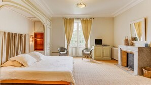 Una habitación de hotel con una cama grande, dos sillones, un televisor, una chimenea y un espejo.