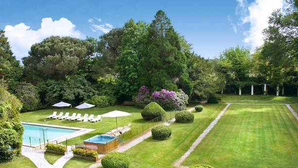 Un jardín cuidado con piscina, sillas de descanso y setos podados.