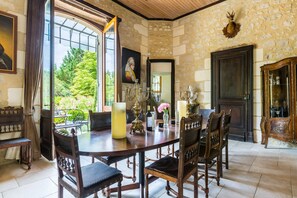 A dining area with a stone wall, a large window, and a view of greenery. - Chateau Seyches - Five Bedroom Castle, Sleeps 10 (Puymiclan)