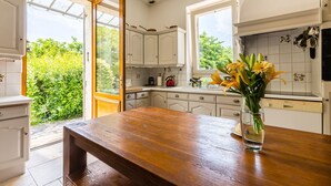 Een keuken met witte kastjes, een houten tafel en een raam met uitzicht op groen.