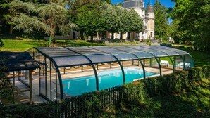 Una piscina con cerramiento de vidrio, rodeada de abundante follaje y un gran edificio con cúpula al fondo.