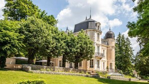 Un edificio grande e histórico con una torre y cúpula destacadas, rodeado de exuberante vegetación y un césped cuidado.
