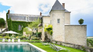A stone building with a pool, surrounded by greenery and a clear sky.