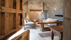 A rustic interior with exposed stone walls, wooden furniture, and a stone fireplace.