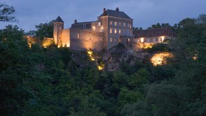 A castle-like building with multiple towers and a large central structure, surrounded by dense forest.