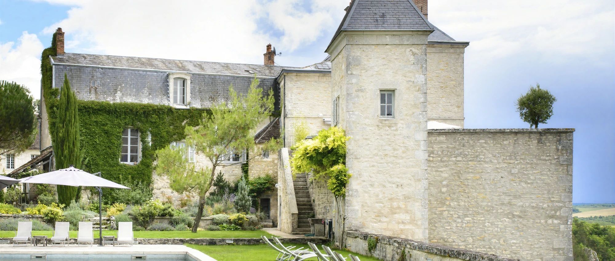 A stone building with a tower, a swimming pool, and outdoor seating.