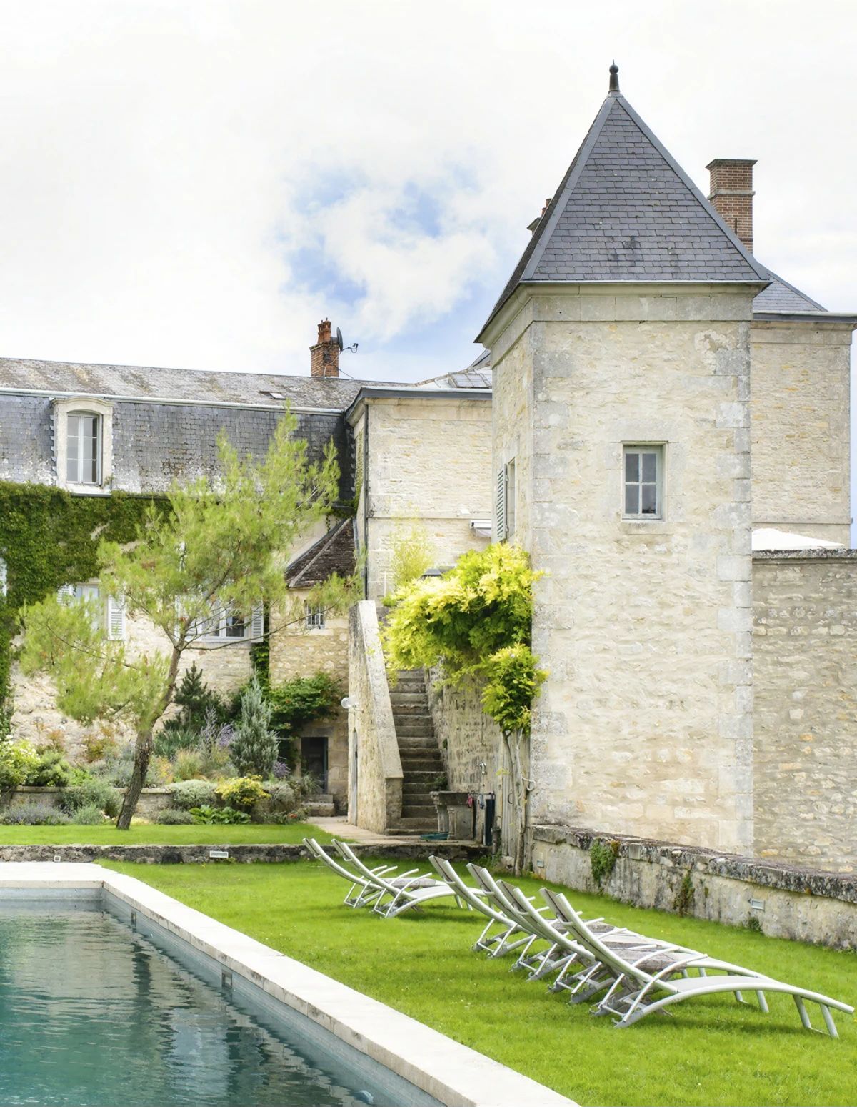 Un bâtiment en pierre avec une piscine et des chaises longues.