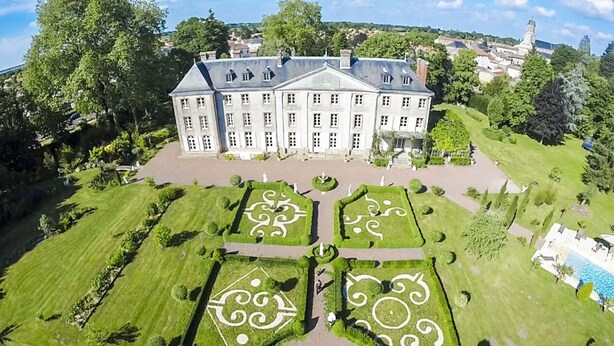 Un edificio grande e histórico con jardines simétricos y una fuente central.