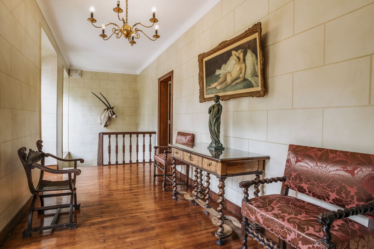 A hallway with wooden flooring, a chandelier, a bench, a table with a vase, and a framed painting on the wall.
