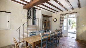 Un coin repas avec une table en bois et des chaises bleues, un escalier et une vue par la fenêtre.
