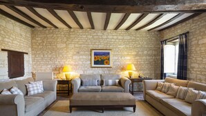 Un salon chaleureux avec des murs en pierre, un plafond en bois, deux canapés, une table basse et deux lampes.