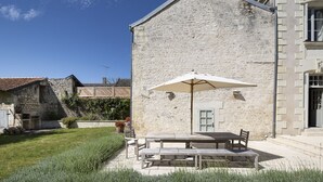 Un bâtiment en pierre doté d’un patio comprenant une table et des chaises, le tout abrité par une marquise.