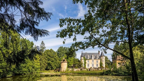 Een historisch gebouw met een groot vijver ervoor, omgeven door weelderige begroeiing.