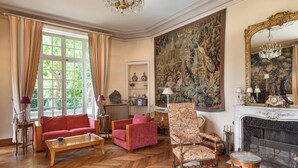 Een ruime woonkamer met een open haard, een groot wandtapijt en klassieke meubels.