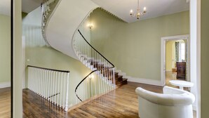 A spacious room with a curved staircase, a white armchair, and a small round table. - Chateau Roussignol - Twelve Bedroom Castle, Sleeps 28 (Le Blanc)