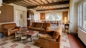 A spacious living room with leather sofas, a wooden coffee table, and a dining area with wooden chairs and a table. - Chateau Roussignol - Twelve Bedroom Castle, Sleeps 28 (Le Blanc)