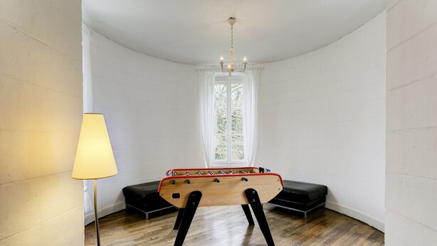A room with a wooden foosball table, a lamp, and a window with white curtains. - Chateau Roussignol - Twelve Bedroom Castle, Sleeps 28 (Le Blanc)