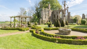 A historic garden with well-manicured hedges, a pergola, and stone ruins.