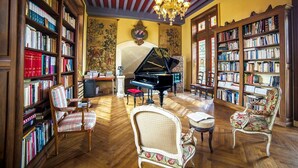 A library with bookshelves, a grand piano, and antique chairs.