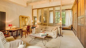 A spacious living room with a sofa, armchairs, a coffee table, and a dining area with a table and chairs. Large windows provide natural light and a view of greenery outside. - The Secret Hamlet - Eleven Bedroom Castle, Sleeps 24 (Ingrandes)