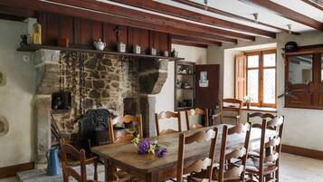 A rustic dining area with a stone fireplace, wooden chairs, and a wooden table.