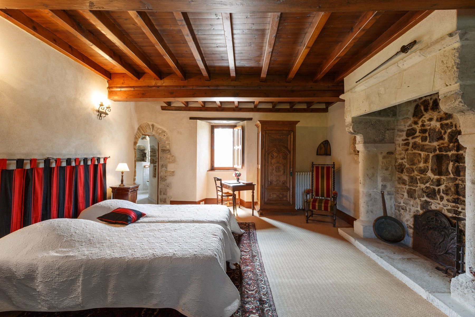 Une chambre traditionnelle avec une cheminée en pierre, deux lits avec du linge de lit blanc, un plafond en bois et un mur en pierre.