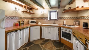 Una cocina con suelo de piedra, microondas, horno, pileta y vigas de madera en el techo.