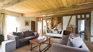 Un salon rustique avec des poutres apparentes, un ensemble de canapés, une table basse et un escalier menant à un autre niveau.