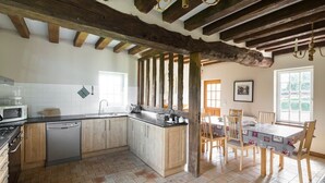 Une cuisine avec des poutres en bois, un lave-vaisselle, une cuisinière et un coin repas comprenant une table et des chaises.