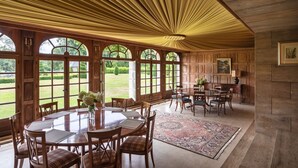 A spacious dining area with a large round table and chairs, a patterned rug, and a view of a well-manicured garden through large windows. - Domaine Du Pont - Chateau Only (Saint-Maclou)