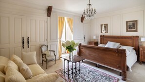 A bedroom with a wooden bed, a chair, a table with a vase of flowers, a chandelier, and a painting on the wall. - Domaine Du Pont - Chateau Only (Saint-Maclou)